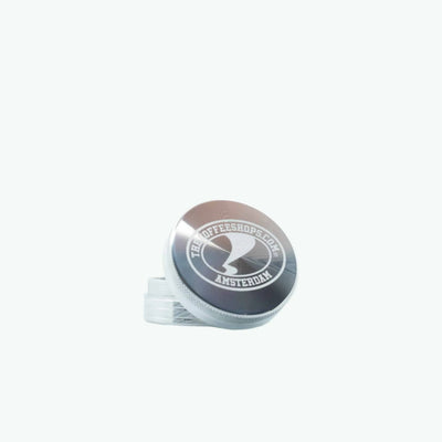 Silver metal grinder by The Coffeeshops with textured surface and grinding teeth, designed for coffee or herbs.